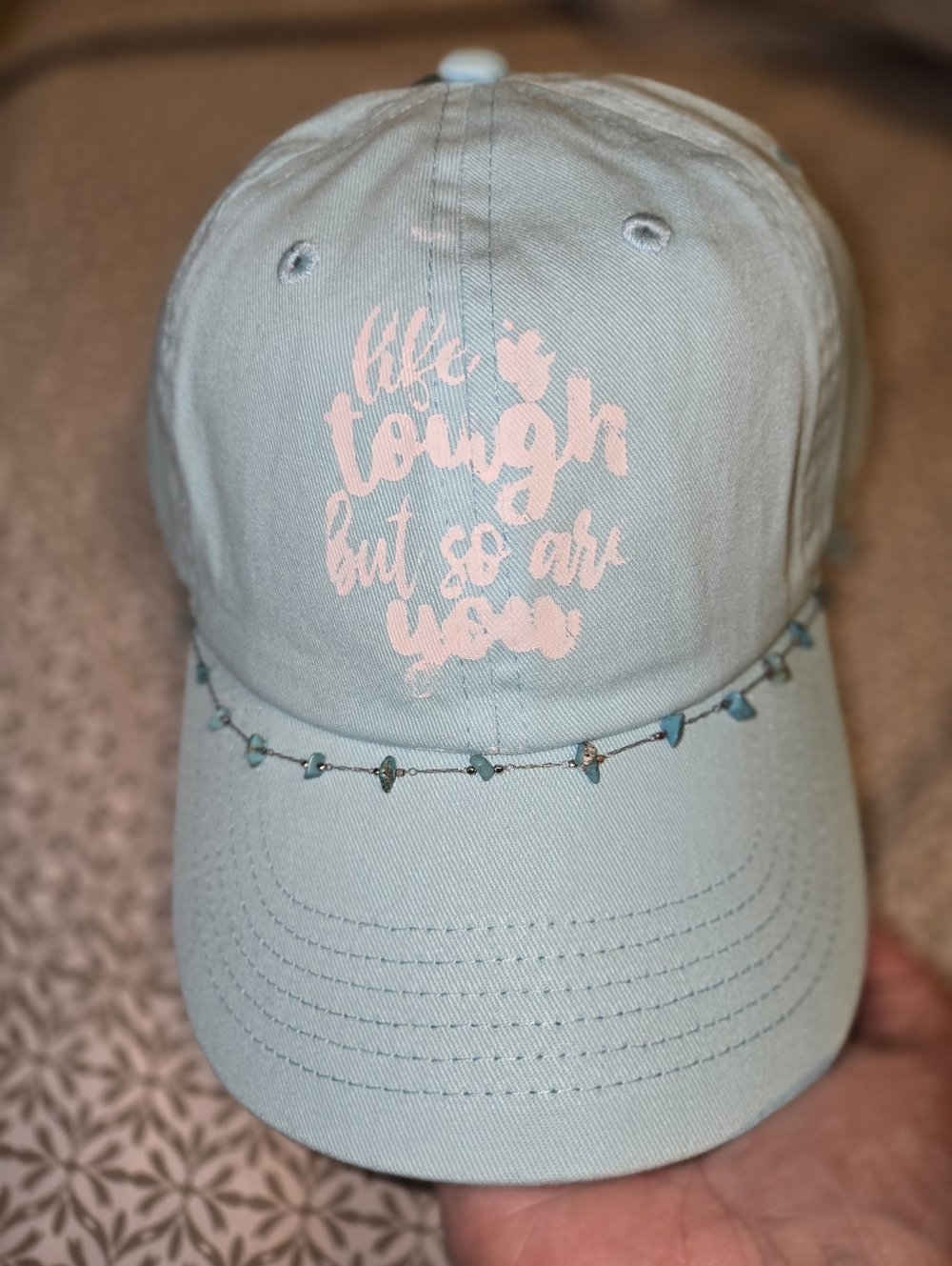 Light Blue Baseball Cap With White Saying And A Boho Style Jewerly.